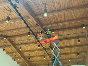 Scenic Solutions technicians safely installing lighting fixtures using an electric scissor lift .